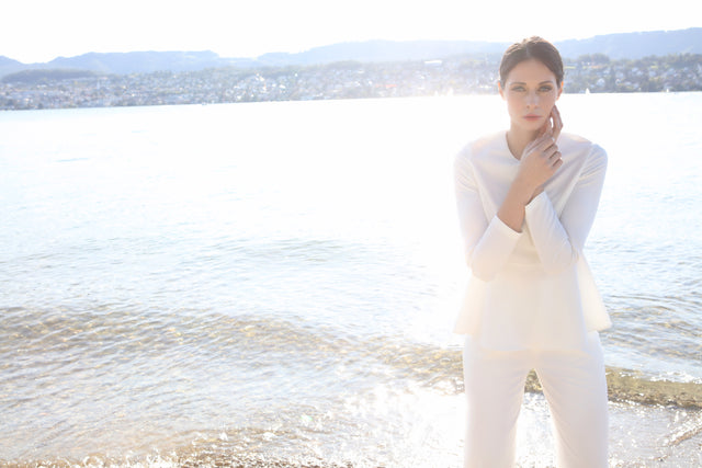 Model wearing white top and white pants in front of lake Zurich